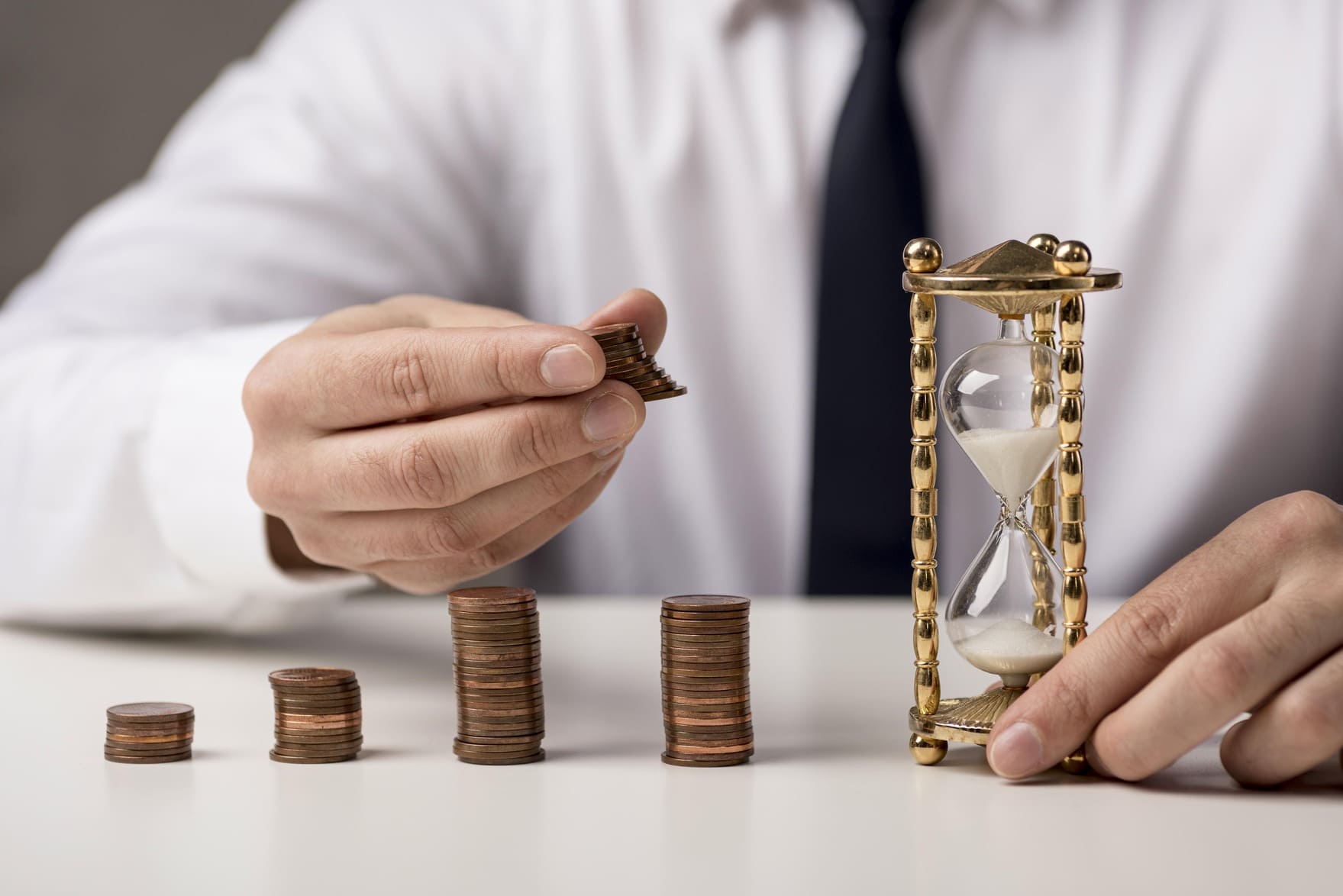 se muestran montones de monedas junto a un reloj de arena